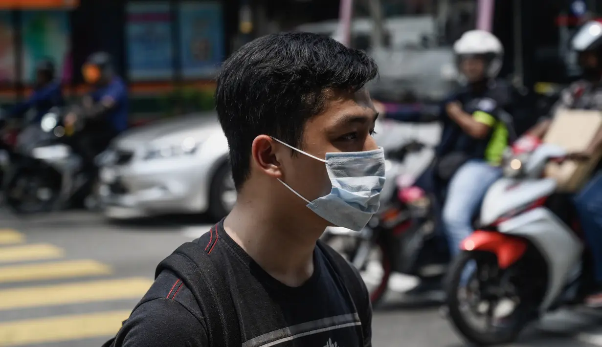 Seorang pria berjalan mengenakan masker saat kabut menyelimuti Kuala Lumpur (10/9/2019). Malaysia tengah mempersiapkan membuat hujan buatan setelah kualitas udara di sejumlah negara bagian mencapai level yang tidak sehat. (AFP Photo/Mohd Rasfan)