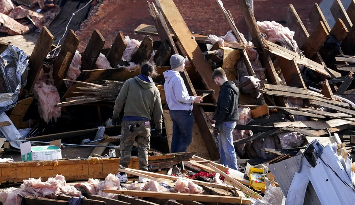Warga memilah puing bangunan yang hancur diterjang tornado di Mayfield, Kentucky, Amerika Serikat, 11 Desember 2021. Selain menewaskan puluhan orang, tornado juga meluluhlantakkan rumah, pabrik. (AP Photo/Mark Humphrey)