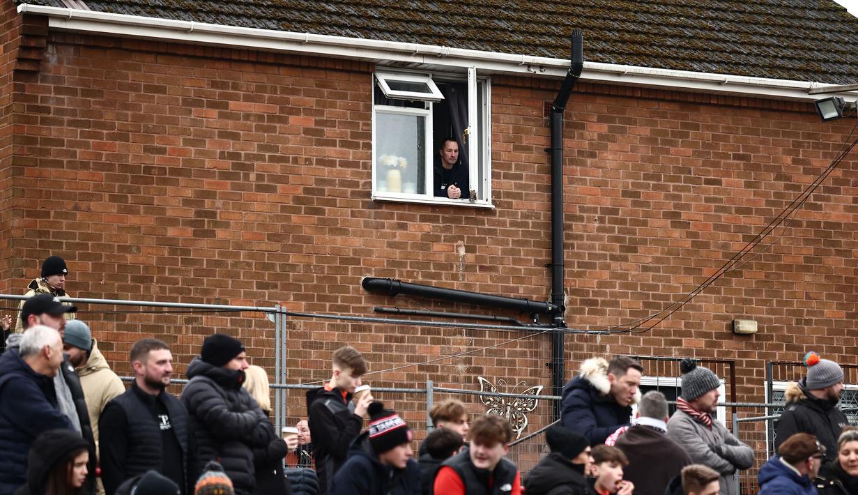 Seorang warga menonton dari jendela pada laga Piala FA 2024/2025 antara Tamworth melawan Tottenham Hotspur di The Lamb Ground, Tamworth, Inggris, Minggu (12/01/2025) waktu setempat. (AFP/Henry Nicholls)