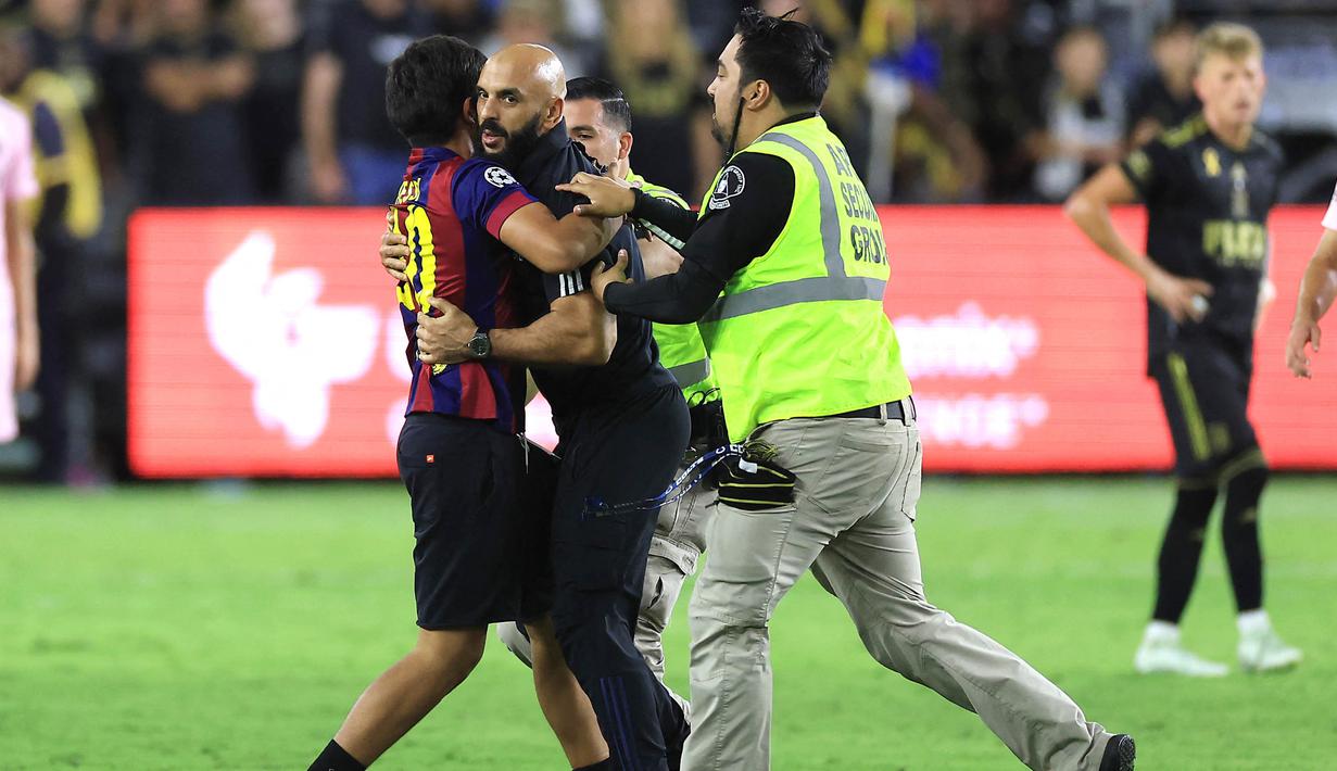<p>Fans itu berlari ke arah Lionel Messi dan mencoba memeluk LM10. Keinginannya itu batal terwujud setelah Yassine Chueko berlari dan menangkapnya. (Sean M. Haffey/Getty Images/AFP)</p>