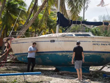 Dua orang pria berdiri dekat sebuah kapal yang terhempas ke daratan akibat terhempas badai Irma di Coconut Grove, Florida, Senin (11/9).Badai Irma menghantam negara bagian Florida dengan kecepatan angin mencapai 200 km/jam. (SAUL LOEB/AFP)