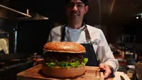 Chef dari restoran The Oak Door, Patrick Shimada berpose dengan burger raksasa di hotel Grand Hyatt Tokyo, Senin (1/4). Golden Giant Burger dibuat untuk memperingati penobatan Putra Mahkota Naruhito pada 1 Mei 2019 dan menandai awal era 'Reiwa' bagi Jepang. (CHARLY TRIBALLEAU/AFP)