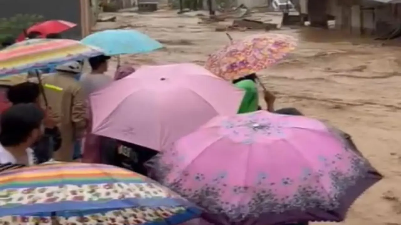 Sejumah warga dengan berpayung menyaksikan aliran banjir luapan Sungai Lubuk Minturun di Koto Tengah Kota Padang, Kamis (27/11/2025).