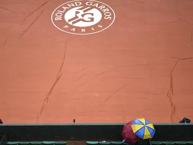 Penonton menggunakan payung menyaksikan lapangan Roland Garros yang ditutup tarpal saat hujan pada turnamen Prancis Terbuka 2016 di Roland Garros, (28/5/2016). (AFP/Philippe Lopez)