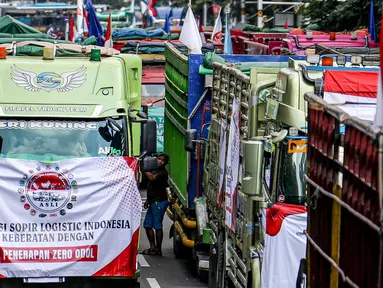 Salah satu peserta aksi terlihat di antara truk-truk saat unjuk rasa terkait Rancangan Undang Undang (RUU) nol kelebihan muatan dan dimensi atau Zero Over Dimension Over Load (ODOL) memasang spanduk di Jalan Medan Merdeka Selatan, Jakarta, Rabu (2/7/2025). (Liputan6.com/Herman Zakharia)