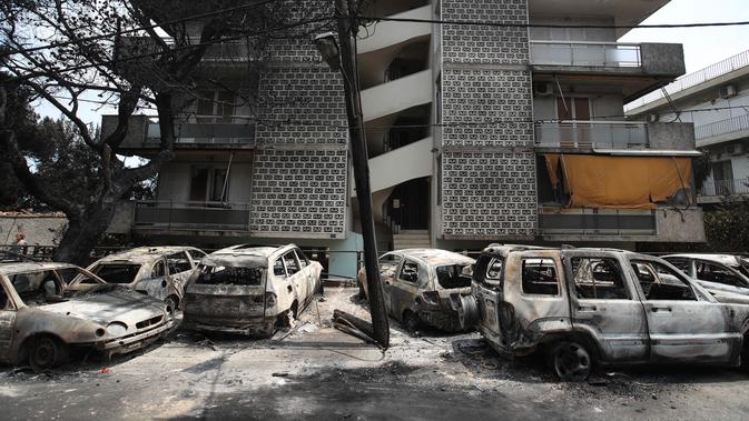 Mobil-mobil yang terbakar berdiri di luar blok apartemen di Desa Mati, timur Athena, Selasa (24/7). Tim penyelamat melaporkan menemukan lebih dari 20 jenazah berkerumun di dekat pantai. (AP Photo/Thanassis Stavrakis)