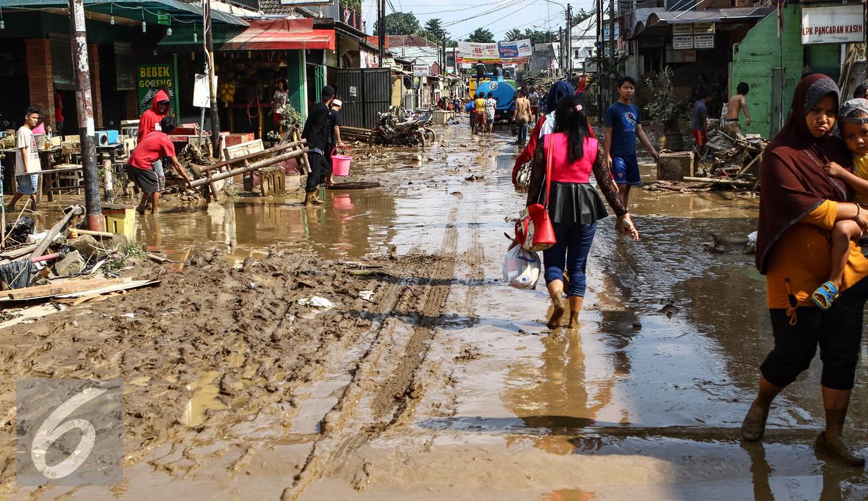 Warga melintas di sepanjang jalan yang dipenuhi lumpur di komplek Pondok Gede Permai Jatiasih, Bekasi, Jumat (22/04). Banjir yang telah merendam ratusan rumah warga mengakibatkan air lumpur mengendap. (Liputan6.com/Fery Pradolo)