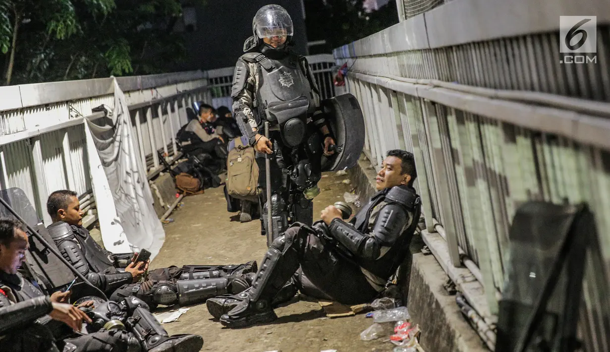 Aparat kepolisan melepas lelah di jembatan penyeberangan orang (JPO) depan Gedung DPR, Jakarta, Selasa (24/9/2019). Mereka melepas lelah usai mengawal demonstrasi mahasiswa menolak pengesahan RUU KUHP dan revisi UU KPK. (Liputan6.com/Faizal Fanani)