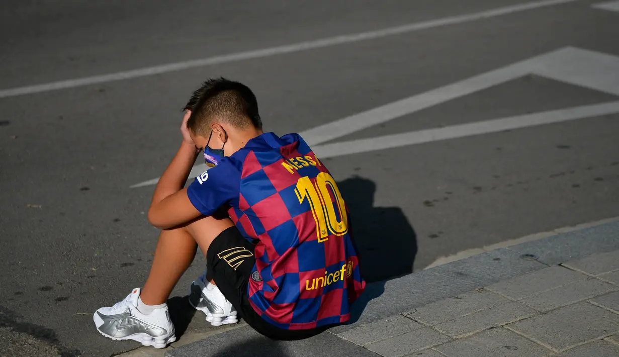 Seorang bocah tertunduk lesu saat menunggu Lionel Messi di lokasi latihan Barcelona, Senin (31/8/2020). Messi secara mengejutkan tidak datang untuk mengikuti tes swab Covid-19 yang dijadwalkan Barcelona. (AFP/Pau Barrena)