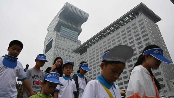 Anak-anak melewati gedung pencakar langit Pangu Plaza di seberang Stadion Olimpiade Bird's Nest, Beijing, Selasa (20/7/2019). Gedung yang pernah masuk dalam film Transformers: Age of Extinction itu terjual dalam lelang online dengan harga 734 juta USD atau sekitar Rp10,5 triliun. (GREG BAKER/AFP)