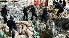 Polisi dari unit pejinak bom menempatkan karung pasir yang mengelilingi bom buatan AS yang dijatuhkan pada Perang Dunia II di persimpangan Convention Avenue dan Hung Hing Road di distrik Wan Chai di Hong Kong (11/5). (Handout / Polisi Hong Kong / AFP)
