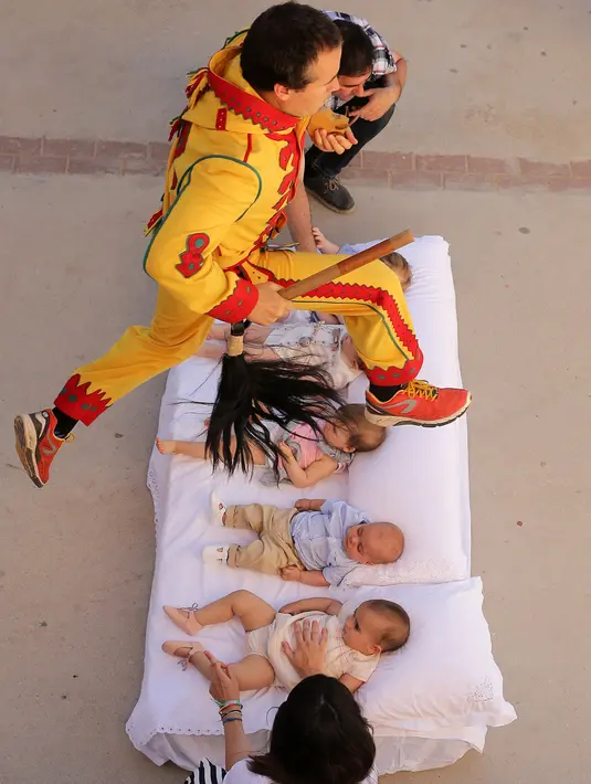 Pria berkostum setan melompati bayi-bayi yang terlentang di atas matras di sebuah jalan selama festival El Colacho di desa Castrillo de Murcia, Spanyol, Minggu (18/6). Festival melompati bayi ini digelar pada bulan Juni tiap tahunnya. (CESAR MANSO/AFP)
