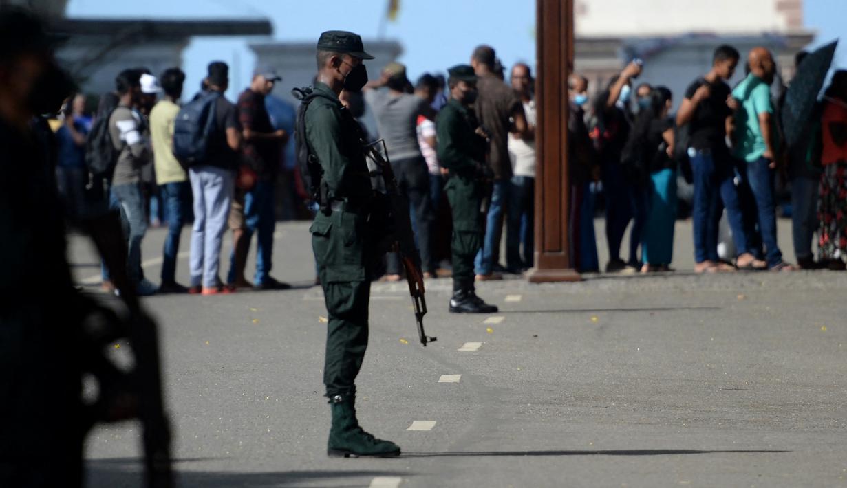 Petugas bersenjata berjaga saat Orang-orang menunggu dalam antrean untuk mengunjungi kediaman resmi presiden Sri Lanka, beberapa hari setelah diserbu oleh pengunjuk rasa anti-pemerintah di Kolombo, Rabu (13/7/2022). Pengunjuk rasa yang kesal menyerbu istana dan kini menjadikannya sebagai spot untuk piknik hingga selfie. (Arun SANKAR / AFP)