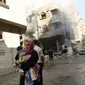 Beberapa warga Palestina berhamburan keluar rumah akibat serangan udara Israel di Gaza, (10/8/2014). Sambil menggendong anak, salah satu warga berlarian menghindari bangunan yang terbakar. (REUTERS/Ahmed Zakot)