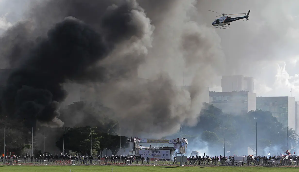 Helikopter terbang saat bentrokan antara pengunjuk rasa anti-pemerintah dengan aparat kepolisian di Brasilia, Brasil, (24/5). Massa yang menuntut pengunduran diri Presiden Michel Temer mengamuk membakar gedung kementerian pertanian (AP Photo/Eraldo Peres)