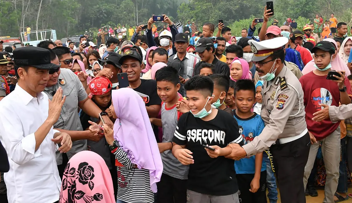 Presiden Joko Widodo atau Jokowi menyapa warga saat memeriksa kerusakan akibat kebakaran hutan dan lahan (karhutla) di Pekanbaru, Riau, Selasa (17/9/2019). Jokowi menegaskan pentingnya menjaga komitmen agar karhutla tak terjadi lagi. (Handout/Indonesian Presidential Palace/AFP)