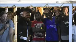 Para imigran melambaikan tangan di kapal Open Arms sebelum turun di pulau Sisilia Lampedusa, Italia (20/8/2019). Jaksa penuntut Italia Luigi Patronaggio memerintahkan penyitaan sebuah kapal penyelamat migran dan evakuasi langsung dari 80 migran yang tersisa di kapal. (AP Photo/Salvatore Cavalli)