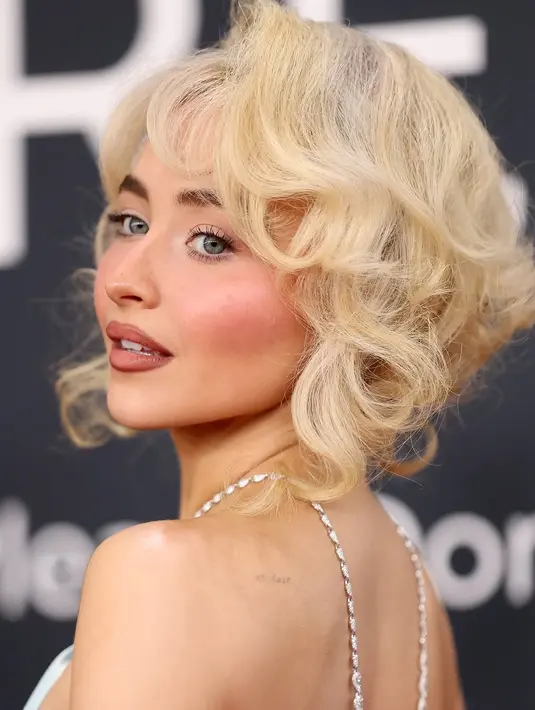 Untuk melengkapi penampilannya, Sabrina mengenakan kalung berlian Chopard seberat 19 karat yang menjuntai di sepanjang punggungnya, anting berlian berbentuk pear, serta cincin berlian oval 10 karat dari perancang yang sama. Gaya ini juga memberikan sekilas tampilan tato kupu-kupu di tulang rusuknya serta tulisan "at last" di bahunya. [@sabrinacarpenter/@mtv].