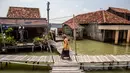 Wilayah daratan yang dulunya mayoritas, kini menjadi lautan akibat penurunan tanah dan kenaikan muka air laut setinggi 25 cm per tahun. Tampak dalam foto, seorang wanita berjalan melintasi jembatan melewati rumah-rumah yang sebagian terendam air laut akibat banjir pasang di desa Timbulsloko, Demak, Jawa Tengah pada Sabtu 18 April 2026. (DEVI RAHMAN/AFP)