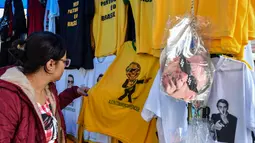 Seorang wanita melihat kaus bergambar Capres Brasil, Jair Bolsonaro dari sayap kanan di sebuah toko pinggir jalan yang populer di Sao Paulo, 8 Oktober 2018. Bolsonaro unggul dalam penghitungan suara pemilu putaran pertama. (AFP/NELSON ALMEIDA)