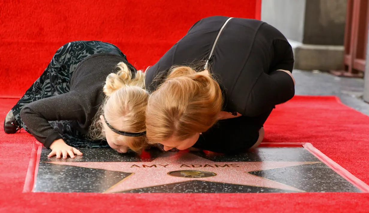Amy Adams bersama anaknya mencium plakat penghargaan dari Hollywood Walk of Fame di Los Angeles, AS, Kamis (12/1). Adams menerima plakat penghormatan atas perannya di film fiksi ilmiah Paramount Pictures Arrival. (AP Photo/ Rich Fury)