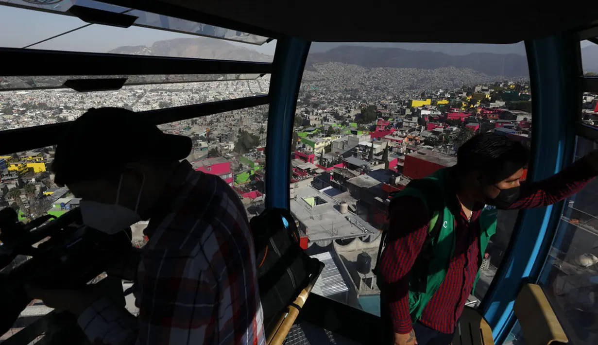 Seorang jurnalis dan seorang pekerja kota melakukan uji coba kereta gantung antara stasiun Campos Revolucion dan Tlalpexco selama peresmian sistem angkutan umum udara baru yang disebut Cablebus di lingkungan Cuautepec, utara Mexico City, Meksiko, Kamis (4/3/2021). (AP Photo/Rebecca Blackwell)