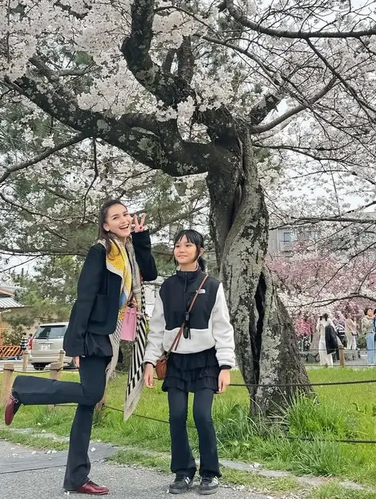 Ayu Ting Ting mengajak putrinya, Bilqis dan orangtuanya ke Jepang. Berfoto di bawah pohon sakura, Ayu Ting Ting mengenakan atasan jaket hitam senada dengan celana flarenya. Dipadukan syal warna kuning. [@ayutingting92]