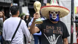 Seorang pedagang kaki lima yang mengenakan topeng gulat tradisional Meksiko memegang suvenir berbentuk piala Piala Dunia di Mexico City, Senin 8 Juni 2026. (Yuri CORTEZ/AFP)