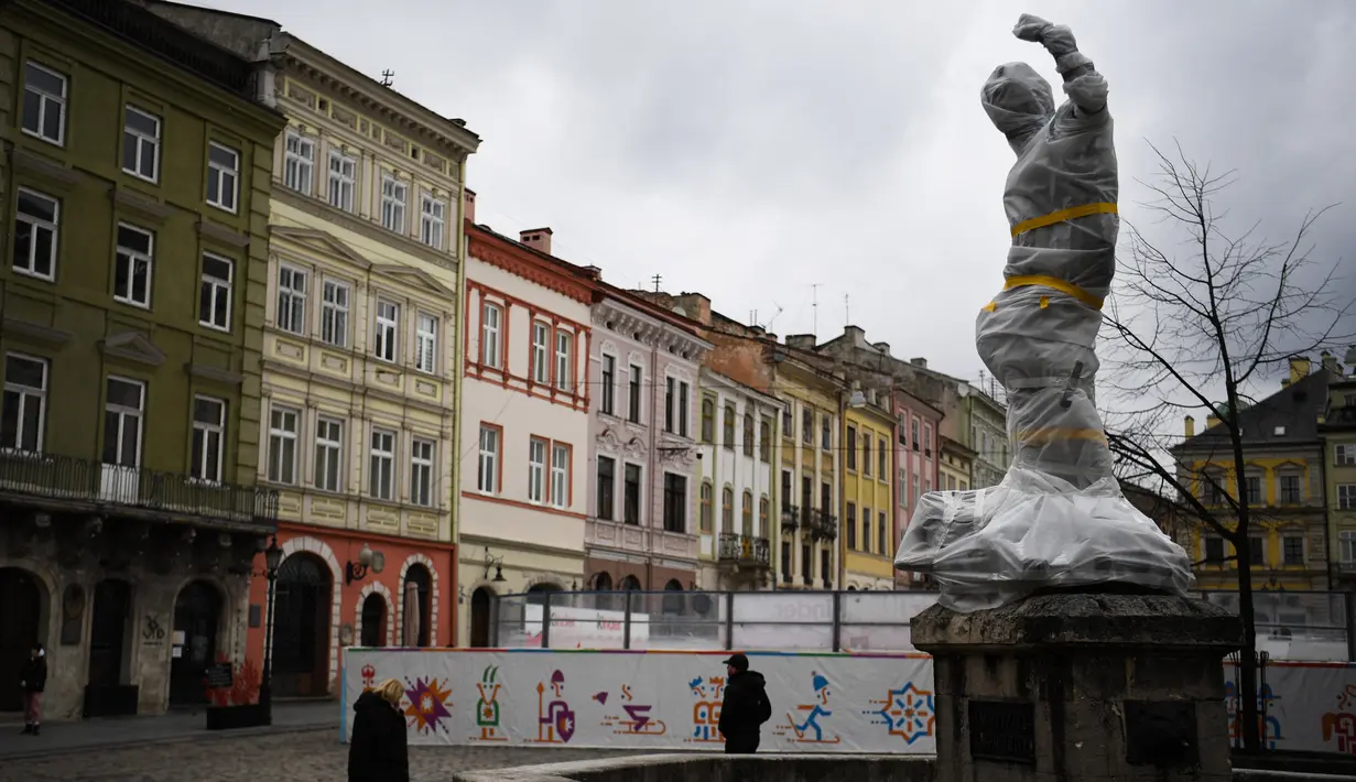 Pejalan kaki berjalan melewati patung yang dibungkus dengan plastik pelindung di dekat dewan kota di Lviv barat Ukraina, pada 5 Maret 2022. Warga kota Lviv membungkus semua patung untuk melindungi warisan sejarahnya dari kerusakan akibat serangan di tengah konflik Rusia-Ukraina. (Daniel LEAL/AFP)