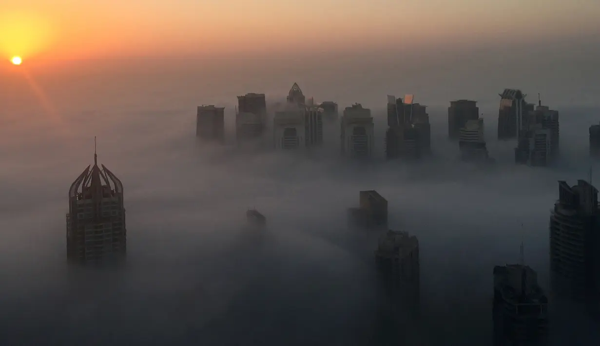 Matahari terbit memancarkan sinar yang berwarna oranye keemasan diantara gedung pencakar langit di Kota Dubai, Uni Emirat Arab, Senin (5/12). Biasanya kabut ini muncul saat musim panas yang terik berubah ke musim dingin yang cukup sejuk. (AFP/Rene Slama)