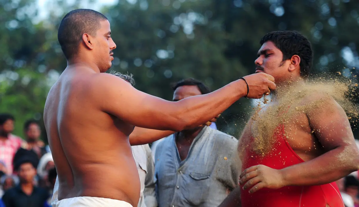 Seorang pria melempari tanah ke pegulat sebelum mengikuti kompetisi gulat tradisional India yang diadakan di desa Rampur, India (7/10). Olahraga tradisional ini terus di lestarikan sebagai bagian dari budaya India. (AFP Photo/Sanjay Kanojia)