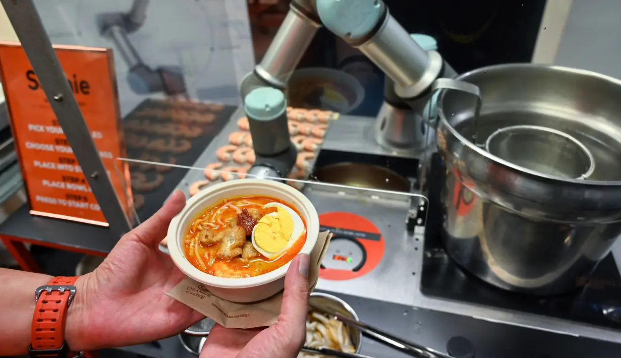 Seseorang memegang semangkuk laksa yang disajikan robot koki bernama Sophie di Singapura pada 26 Juli 2019. Pihak perusahaan menjamin, tidak ada rasa yang berbeda dari laksa buatan robot Sophie maupun buatan koki pada umumnya. (Roslan RAHMAN / AFP)