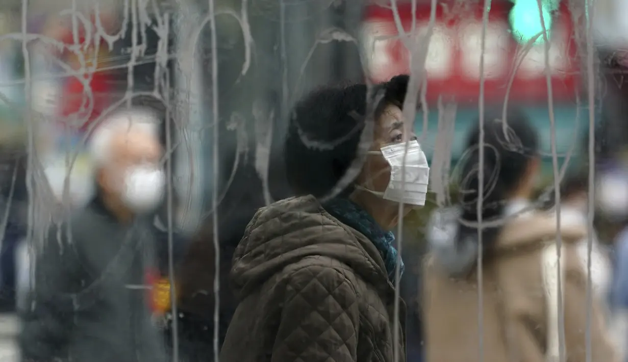Seorang perempuan yang mengenakan masker terlihat melalui jendela kaca yang tercoret-coret saat berjalan di sepanjang penyeberangan pejalan kaki di Shibuya, Tokyo, Selasa (5/1/2021). Tokyo mengonfirmasi lebih dari 1.200 kasus virus corona COVID-19 baru pada Selasa (5/1). (AP Photo/Eugene Hoshiko)