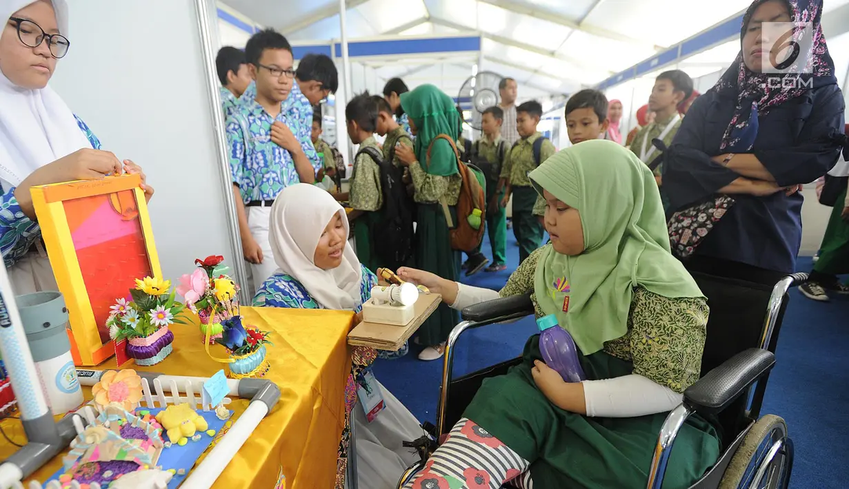 Seorang murid SD berkursi roda mendapatkan penjelasan cara kerja dinamo mekanik yang dapat menimbulkan listrik dari murid SMPN 3 Tangsel saat kegiatan PIF 2018 di kawasan Puspiptek, Setu, Tangerang Selatan, kamis (27/9). (Merdeka.com/Arie Basuki)