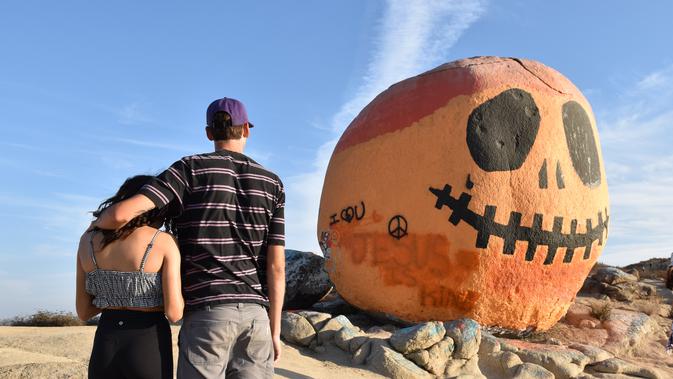 Orang-orang mengunjungi Pumpkin Rock (Batu Labu) di puncak sebuah bukit di Norco,  California, AS (18/10/2020). Menjelang perayaan Halloween, Pumpkin Rock, sebongkah batu raksasa yang dilukisi seperti Jack-O'-Lantern besar, menjadi objek wisata yang populer bagi pengunjung. (Xinhua/Gao Shan)