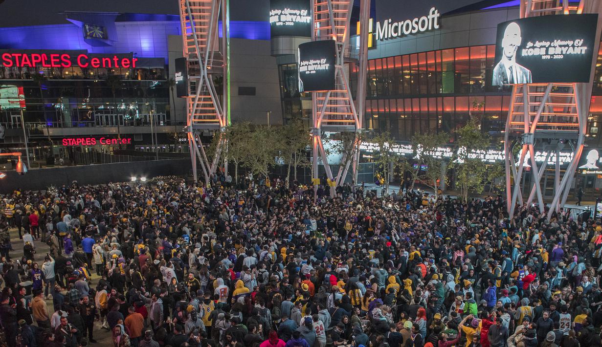 Sejumlah warga berkumpul untuk mengenang wafatnya Kobe Bryant di Staples Center, Los Angeles, Minggu (26/1). Akibat kecelakaan helikopter, legenda NBA itu wafat bersama sang putri. (AFP/Apu Gomes)