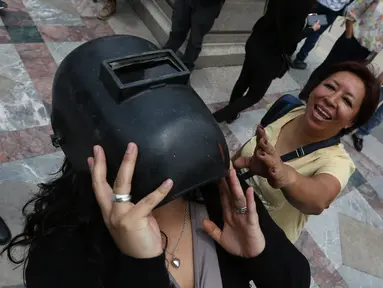 Seorang wanita mengenakan helm las untuk melihat gerhana matahari parsial di Mexico City, Senin (21/8). Gerhana matahari total terjadi di 14 negara bagian AS, sementara lainnya mengalami gerhana matahari parsial. (Gustavo Martinez Contreras/AP)