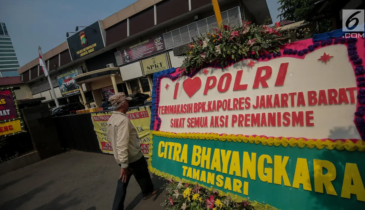 Warga melintasi karangan bunga di Halaman Polres Jakarta Barat, Jumat (23/11). Puluhan karangan bunga yang dikirimkan warga tersebut diberikan guna mendukung pihak kepolisian dalam memberantas aksi premanisme di Jakarta Barat. (Liputan6.com/Faizal Fanani)
