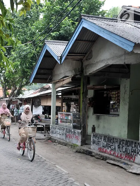 Dua bocah bersepeda melintasi coretan protes di salah satu tembok rumah di Pulau Pari, Kepulauan Seribu, Jakarta, Minggu (29/4). Coretan dibuat warga yang menolak klaim PT Bumi Pari Asri atas kepemilikan lahan Pulau Pari. (Merdeka.com/Iqbal S. Nugroho)