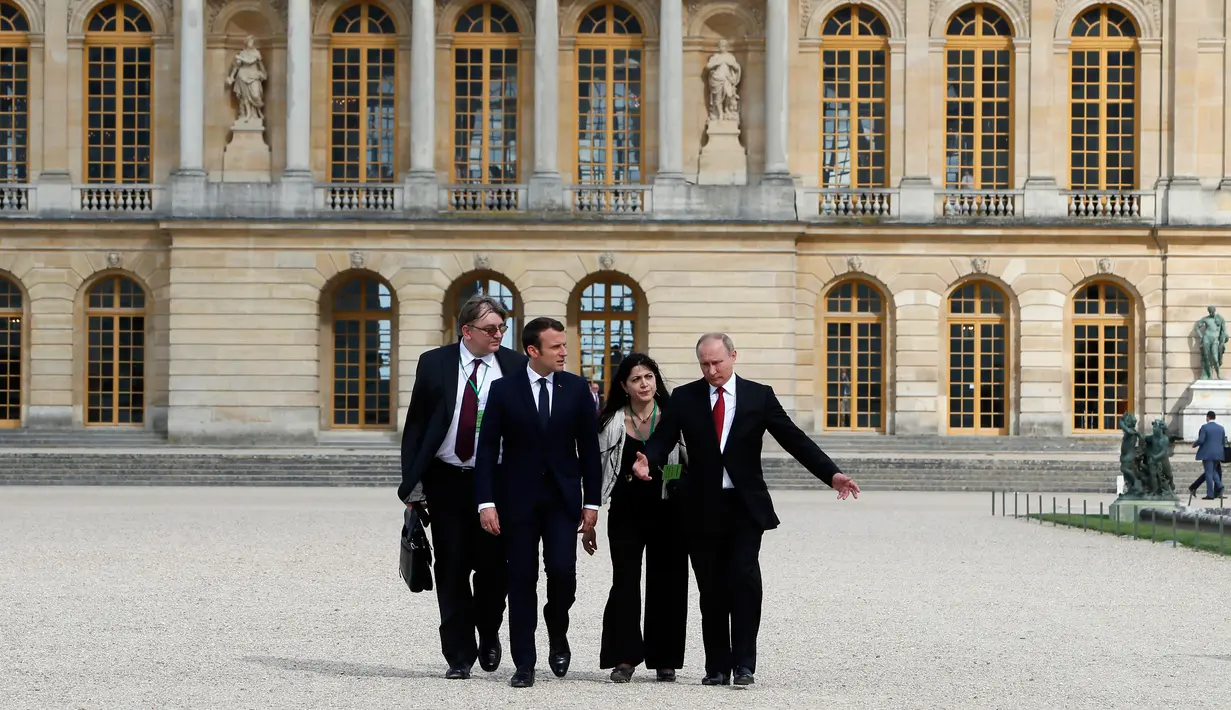 Presiden Prancis Emmanuel Macron dan Presiden Rusia, Vladimir Putin didampingi juru bicara masing-masing menuju taman Istana Versailles, dekat Paris, setelah mereke menggelar pertemuan, Senin (29/5). (AP Photo/Francois Mori, pool)