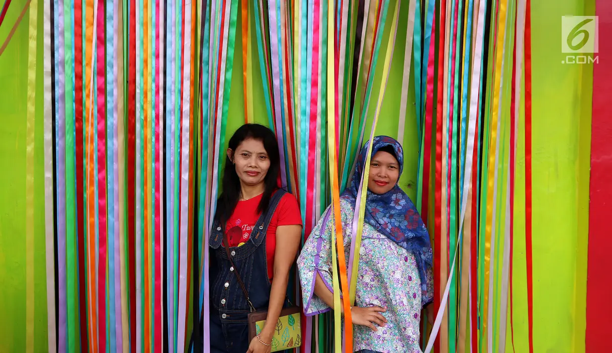 Dua wisatawan berpose di balik pita di kampung warna-warni, Kelurahan Kesatrian, Kota Malang, Minggu (5/11). Lukisan di kampung tersebut melibatkan komunitas mural dan seniman. (Liputan6.com/Fery Pradolo)