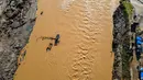 Rakit tali tersebut tak hanya mengangkut orang dewasa, tetapi juga sepeda motor. Tampak dalam foto, pemandangan udara menunjukkan orang-orang menyeberangi sungai Peusangan menggunakan rakit setelah banjir bandang yang menghancurkan desa-desa di sekitarnya di Kabupaten Bireuen, provinsi Aceh, pada Senin 5 Januari 2026. (CHAIDEER MAHYUDDIN/AFP)