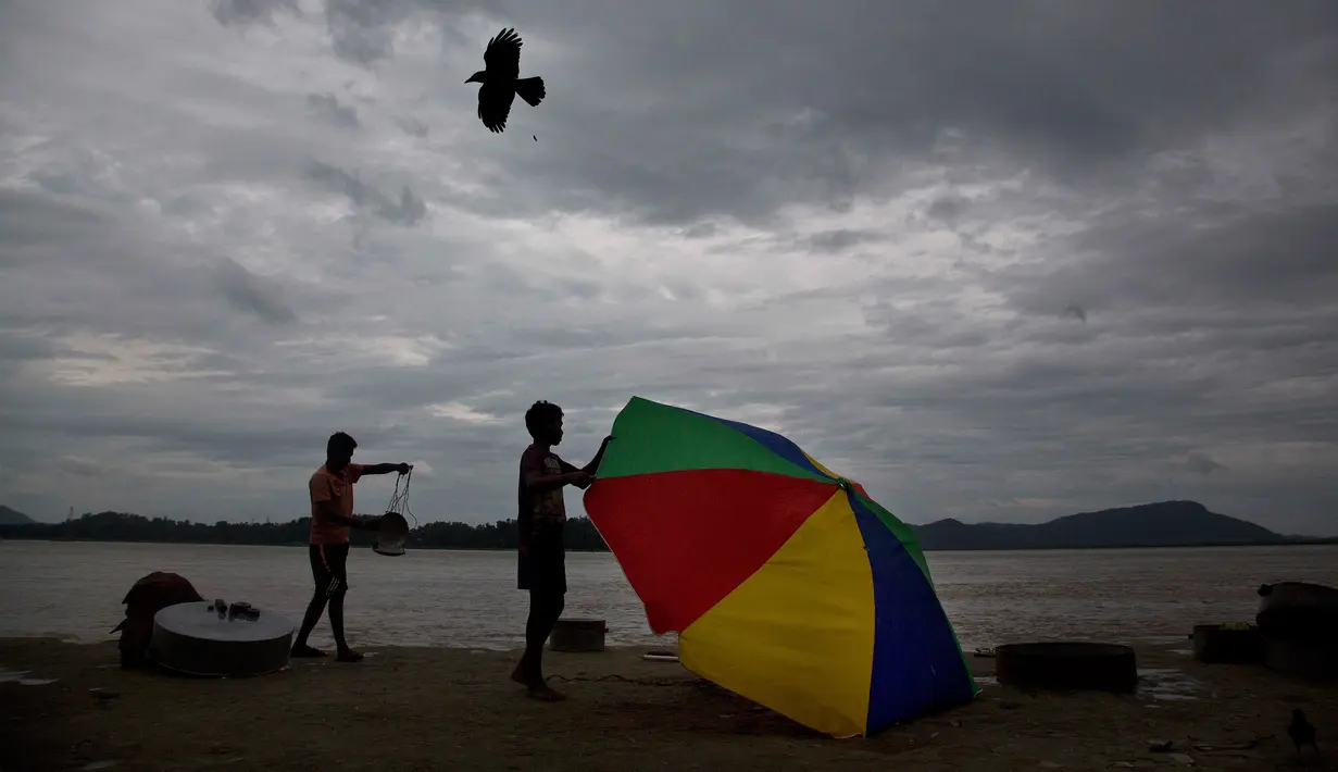 Seorang penjual ikan memegangi payungnya yang tertiup angin di tepi sungai Brahmaputra, India, Selasa (30/5). Beberapa negara bagian di India timur laut mengalami hujan deras sebagai efek topan Mora yang melanda selatan Bangladesh. (AP Photo/Anupam Nath)