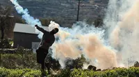 Seorang pemuda Palestina mengembalikan tabung gas air mata ke arah pasukan keamanan Israel saat bentrok pada demonstrasi menentang pengambilalihan tanah oleh Israel dekat pemukiman Yahudi Kedumim di Desa Kfar Qaddum, Tepi Barat, 21 Januari 2022. (JAAFAR ASHTIYEH/AFP)
