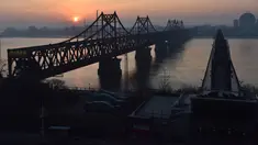 Matahari terbit di belakang Jembatan Persahabatan yang membentang Sungai Yalu antara China dan Korea Utara terlihat dari kota Dandong di provinsi Liaoning timur laut China (22/2). (AFP Photo/Greg Baker)