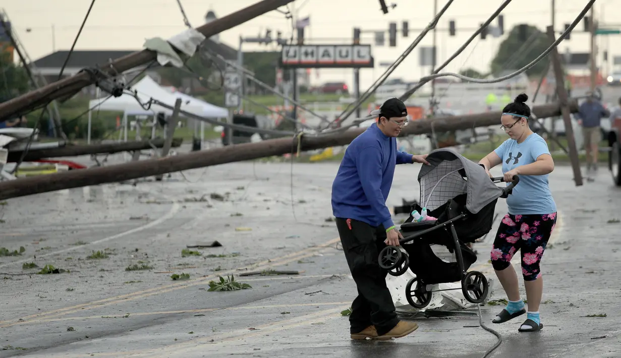 Warga membawa kereta dorong melewati tiang listrik yang berjatuhan usai tornado melanda Jefferson City, Missouri, AS, Kamis (23/5/2019). Tornado juga menghantam ibu kota negara bagian, membawa hujan lebat, hujan es, angin, dan kilat. (AP Photo/Charlie Riedel)
