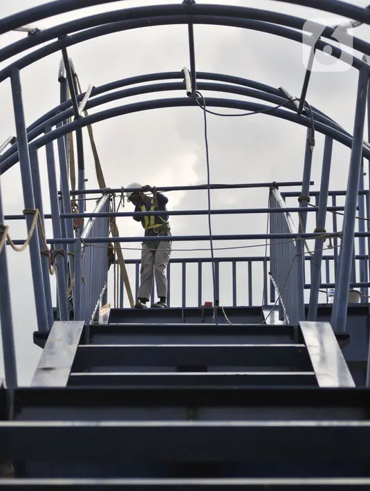Pekerja menyelesaikan pembangunan jembatan penyeberangan orang (JPO) di dekat Stasiun Jatinegara, Jakarta, Senin (11/5/2020). JPO yang ditargetkan rampung pada tahun ini tersebut sekaligus menjadi jalur keluar penumpang kereta Stasiun Jatinegara. (merdeka.com/Iqbal S. Nugroho)