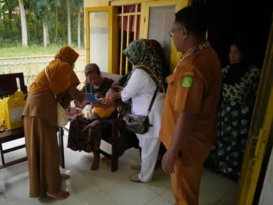 Tenaga kesehatan Siti Nurjanah (kiri) dibantu rekan-rekannya memberikan vaksin campak kepada seorang anak dalam kampanye vaksinasi campak dari rumah ke rumah menyusul wabah di Sumenep, Pulau Madura, Jawa Timur, Senin 8 September 2025. (AP Photo/Dita Alangkara)