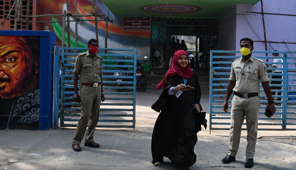 Polisi berjaga-jaga ketika seorang siswa sekolah menengah negeri dan perguruan tinggi pra-universitas untuk wanita melangkah keluar untuk mengembalikan telepon kepada orang tuanya yang berdiri di luar tempat institut pendidikan di Bangalore (16/2/2022). (AFP/Manjunath Kiran)