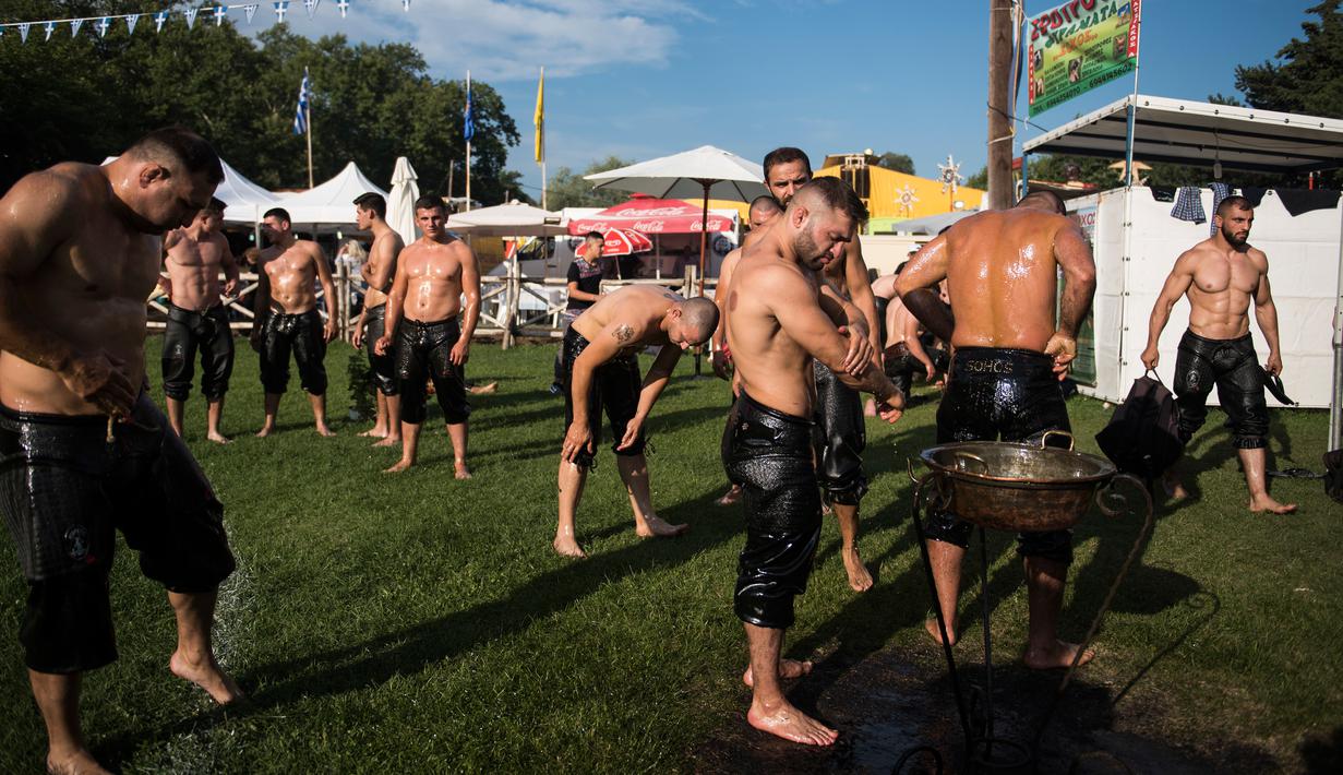Para pegulat melumuri tubuh mereka dengan minyak zaitun sebelum kompetisi tahunan gulat minyak tradisional di Sochos, Yunani, 30 Juni 2018. Pertandingan perpaduan tradisi Yunani kuno dan zaman modern itu diiringi musik tradisional. (AP/Giannis Papanikos)